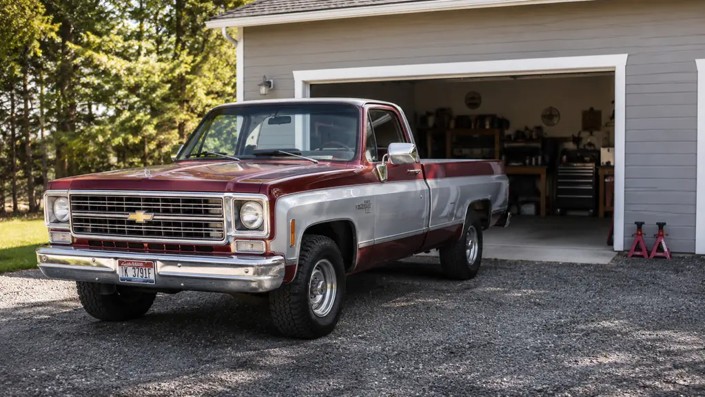 A pickup truck parked in a driveway outside a two-car garage with the door open